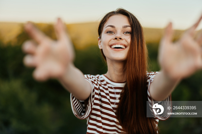 A woman smiles and pulls her hands to the camera close-up in nature with a view of the mountains. Happy travel lifestyle follow me