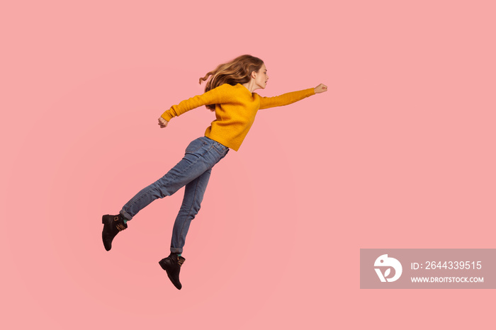 Superpower. Portrait of determined serious ginger girl in sweater and denim flying in air forward to victories, superhero feeling free and confident to achieve goal. indoor studio shot pink background