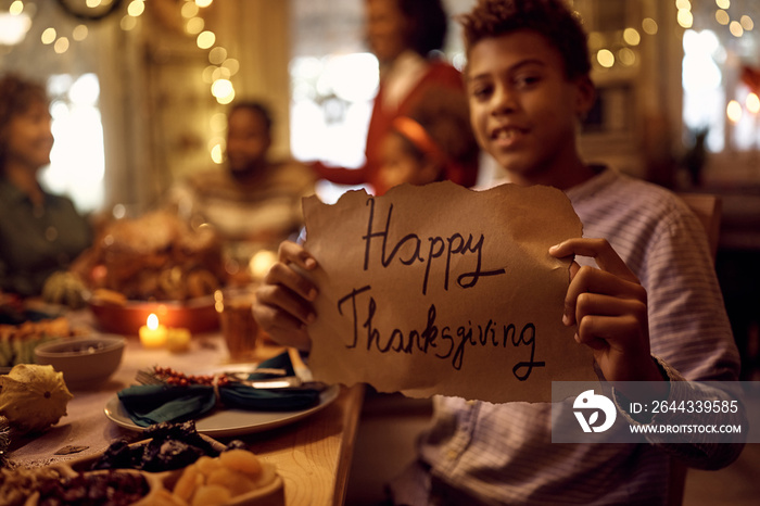 Close up of black kid holding Happy Thanksgiving sign and looking at camera.