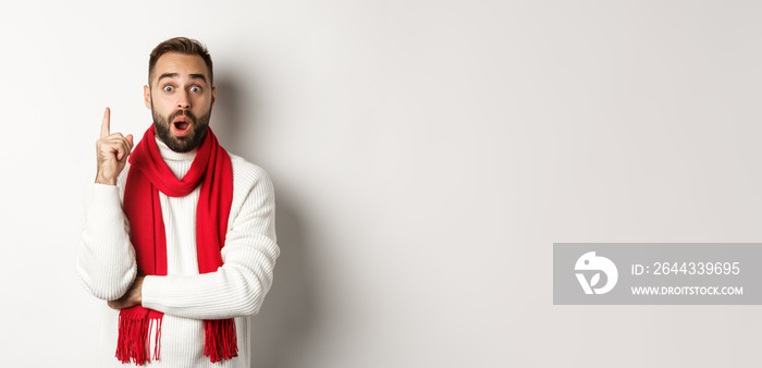 Christmas holidays and celebration concept. Excited bearded man having an idea, raising finger and suggesting plan, standing in red scarf with sweater, white background