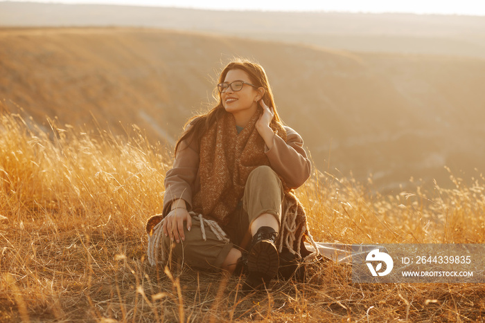 Young smiling woman is sitting on the ground on a sunny late fall day.