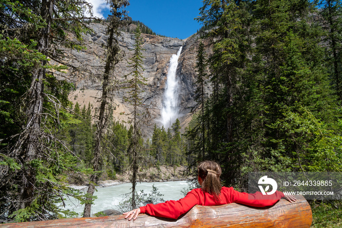 Woman sits on a bench, enjoying the view of Takakkaw Falls in Yoho National Park - British Columbia, Canada