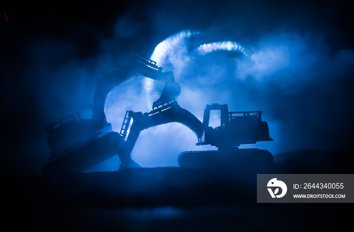 Construction site on a city street. A yellow digger excavator parked during the night on a construction site. Industrial concept table decoration on dark foggy toned background.