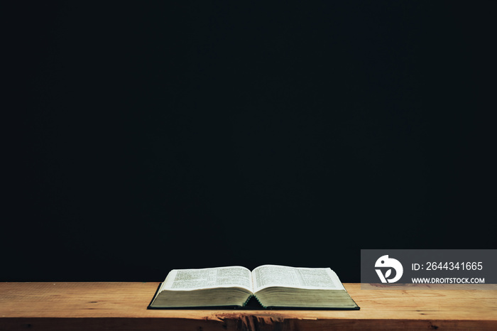 Open Holy Bible on a red old wooden table. Beautiful Black wall background..