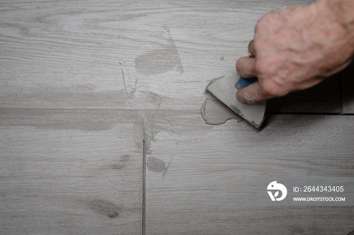 jointing of floor tiles. Grouting tiles seams with a rubber trowel. Grouting ceramic tiles. Tilers filling the space between tiles using a rubber trowel.