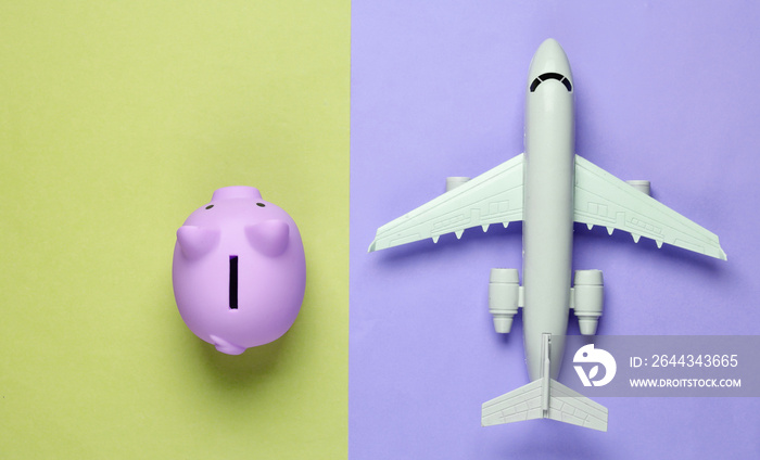 Save up for air travel. Piggy bank, airplane on colored background. Top view. Flat lay