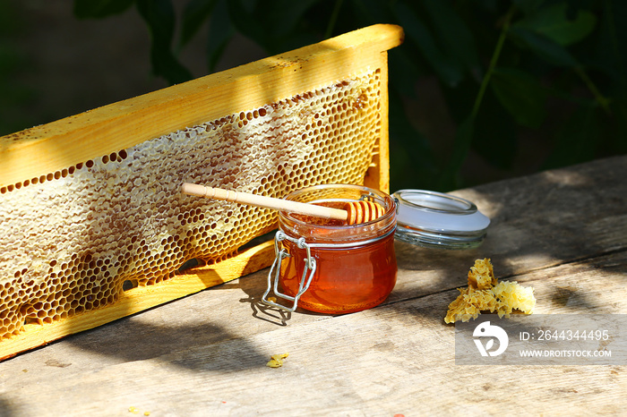 jar of fresh honey in a glass jar on an old table on a apiary. outside. frame with bees wax structure full of fresh bee honey in honeycombs. Beekeeping concept. Top view. Copy space