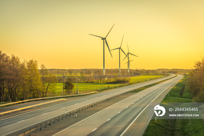 Picture of wind farm generators in the green field close to the road with cars at the sunset