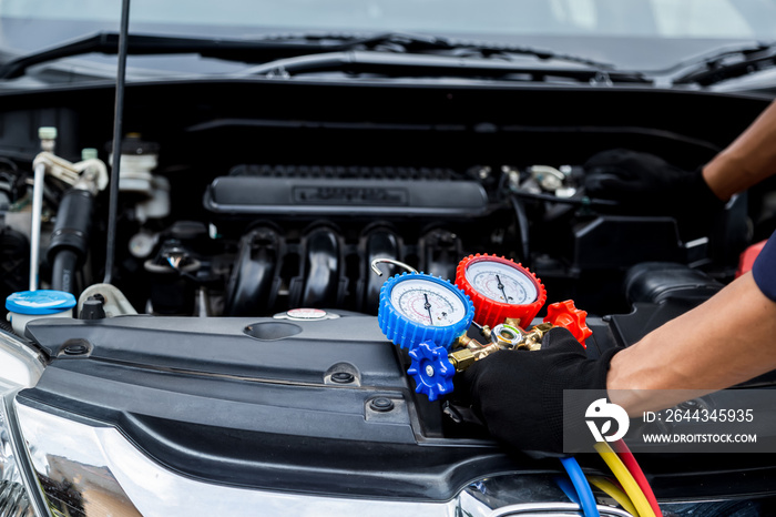 Close up hand of auto mechanic are to use measuring manifold gauge for filling car air conditioners. Concepts of fix and checking for repair service , Car service concept .