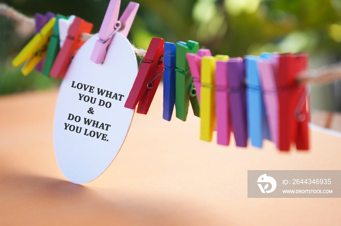 Inspirational and motivational quote - Love what you do and do what you love. Passion concept with text on white circle paper and colorful clips on rope on soft orange and green bokeh light background