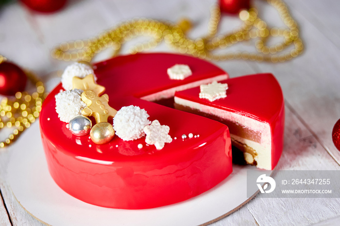 Mousse Christmas pastry cake dessert covered with red mirror glaze with new year decorations on garland lamps bokeh white background, Modern european cake Christmas theme. .