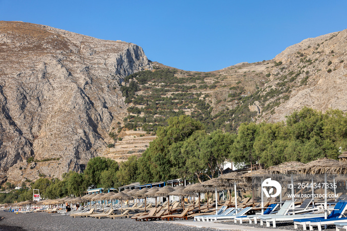 : Sun loungers on the black volcanic beach of Kamari in Santorini. Cyclades, Greece