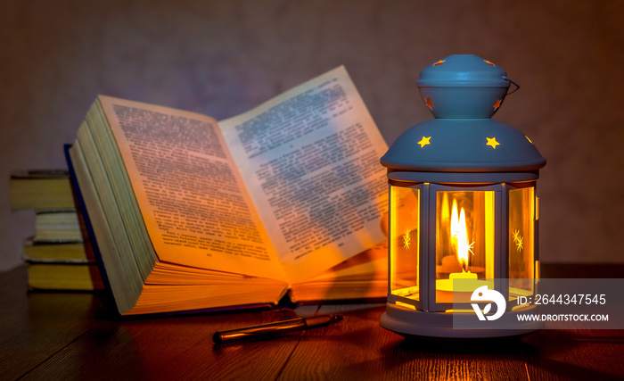 Reading a book at the light of a lantern. Lantern with a lit candle near the unfolded book_