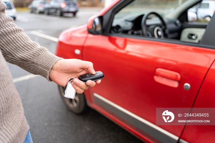 Male hand of young man holding electronic remote key pushing button near red rental car to open or close it. Travel, tour, tourism, journey, mode of transport, technology, ecology, car sharing.