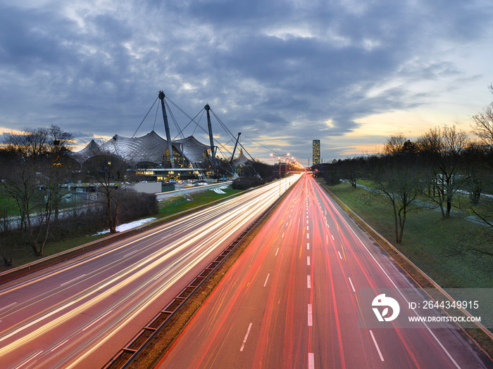 Light trails of cars driving/commuting past modern architecture in a city - Munich, Germany