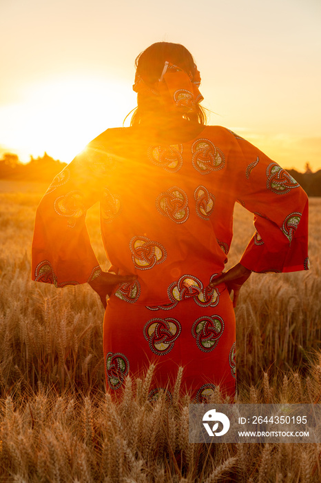 African woman in traditional clothes standing in a field of crops at sunset or sunrise