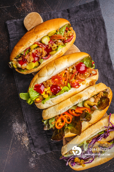 Hot dogs with assorted toppings on a dark background, top view.