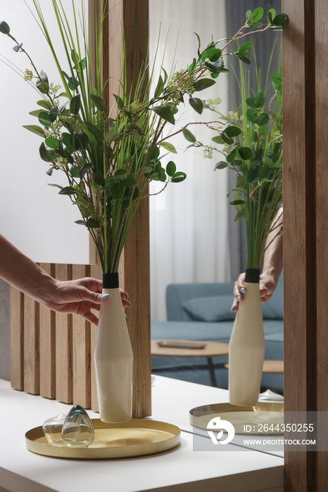 Woman arranging vase with flowers on table. Housewife taking care of coziness in apartment. Interior decor, household and home improvement concept.