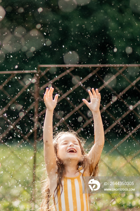 a little smiling girl is happy with the drops of water falling on her like rain on a hot summer day