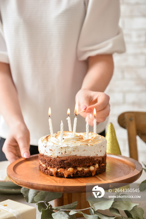 Woman lighting candles on tasty birthday cake at table