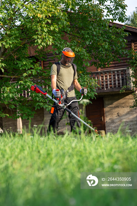 Landscape maintenance concept. Man cutting grass in yard by using electric string grass trimmer.