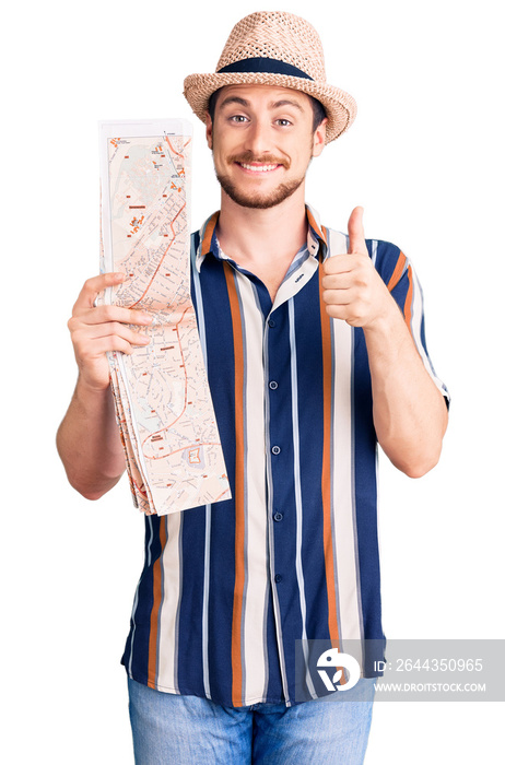 Young handsome caucasian man wearing summer hat holding city map smiling happy and positive, thumb up doing excellent and approval sign