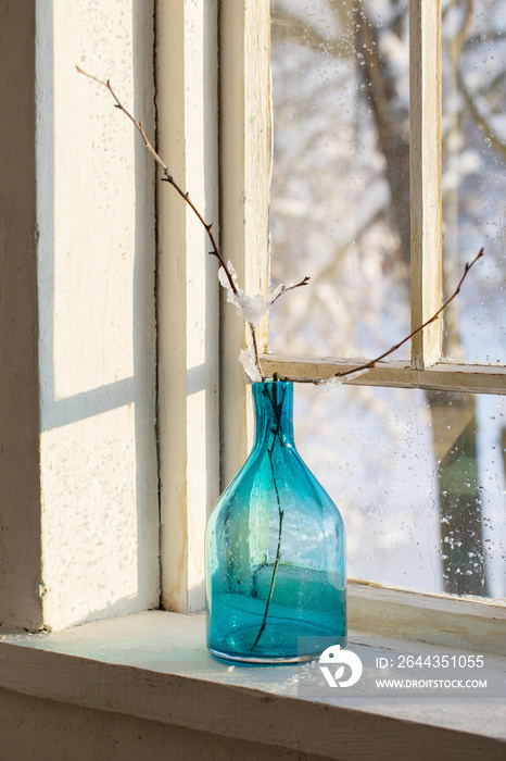 blue glass bottle with branch on old winter window