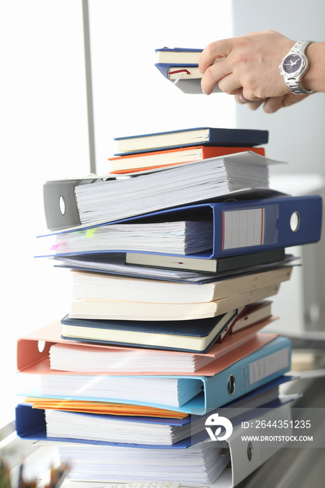 Close up of employee holding stack of old documents and folders while working in his office. Work and business concept