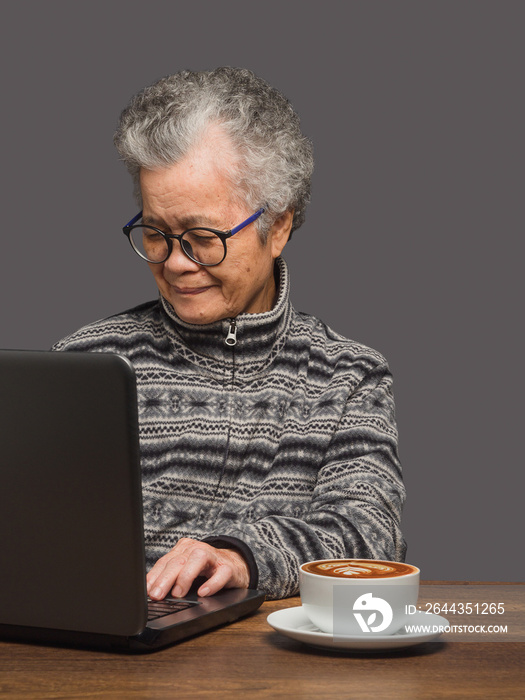 An elderly Asian woman uses a laptop to search for data from the internet while sitting at the table