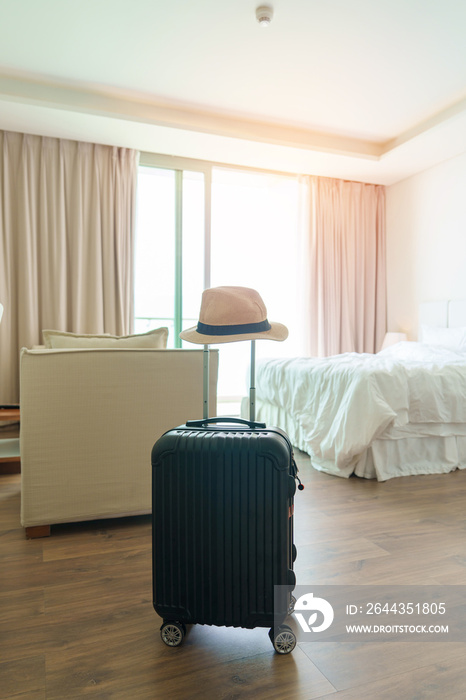 Black Luggage with hat in modern hotel room after door opening. Baggage for Time to travel, service, journey, trip, summer holiday and vacation concepts