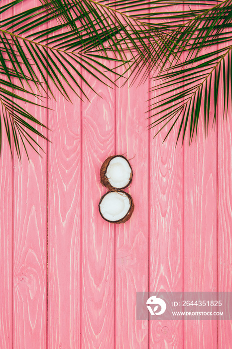 top view of halved coconut and palm leaves on pink wooden surface