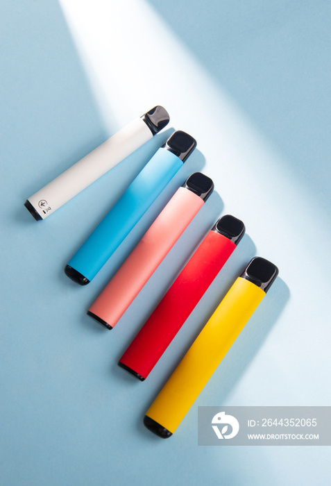 Set of colorful disposable electronic cigarettes on a blue background with hard light. The concept of modern smoking. Top view