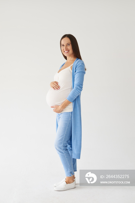 Stylish pregnant woman with hands on belly posing at camera