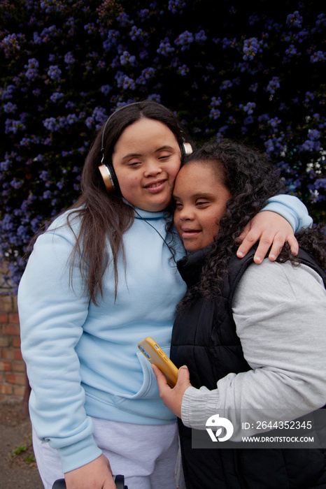 Two curvy women with Down Syndrome hugging in front of flowers