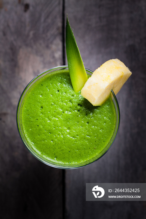 A glass of green smoothies, decorated with leaf and a piece of pineapple.