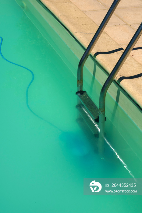 Swimming pool maintenance - An automatic robot pool cleaner can just be seen on the bottom of a cloudy swimming pool removing debris and algae.