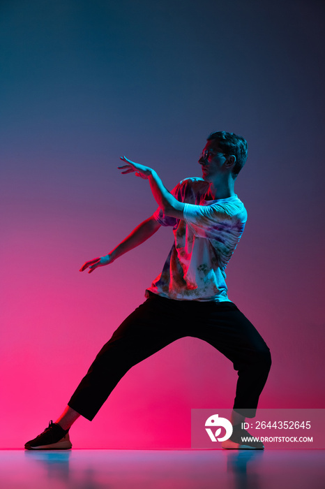 Vertical portrait of young man dancing hip-hop isolated over gradient pink purple background in neon light