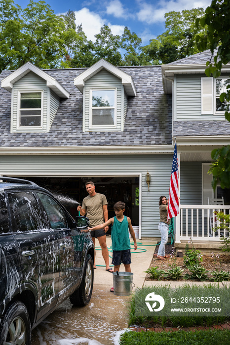 Air Force service member washes his vehicles with his sons in the driveway.