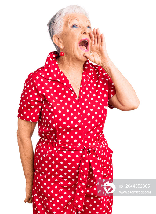 Senior beautiful woman with blue eyes and grey hair wearing a red summer dress shouting and screaming loud to side with hand on mouth. communication concept.