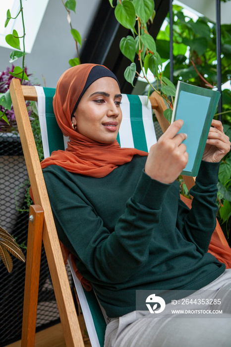 Woman wearing headscarf reading book at home