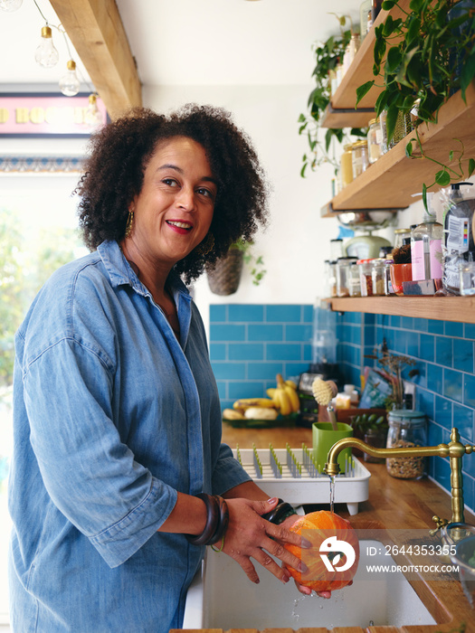 Woman washing pumpkin in kitchen sink