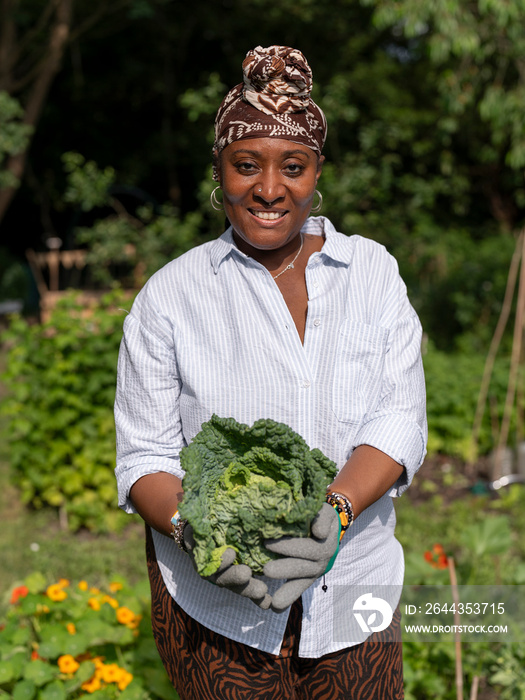 Portrait of smiling mature woman holding cabbage in allotment