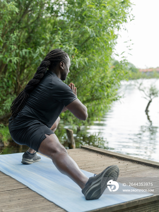 Man practicing yoga by lake