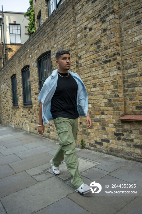 Man wearing unbuttoned shirt and cargo pants walking along brick wall