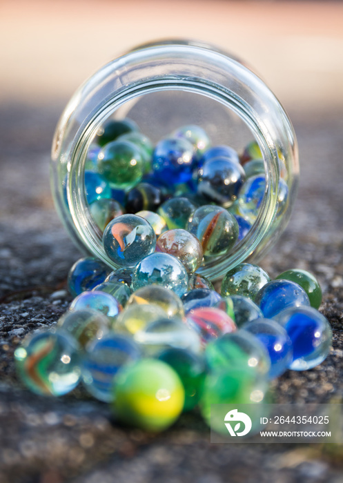 Glass jar full of crushers, fallen on the street. Front view of jar.  Bright picture, with blue as main color.  Front and background blurred.  Other colors red, green, yellow.