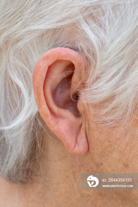 Hearing aid. Female pensioner with white hair wearing a Behind The Ear, BTE, hearing aid. Close up of ear device almost invisible.