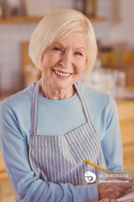 Place your order. Beautiful senior woman in a striped apron working as a waitress in a cafe and posing while making notes about her clients order