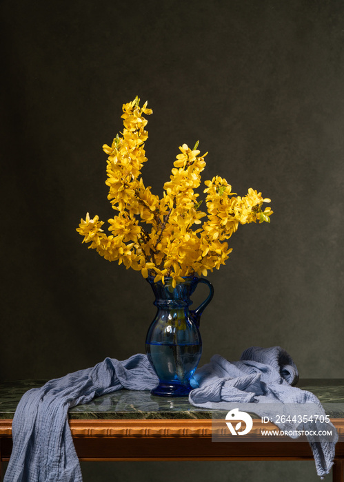 Yellow branches. Bouquet of flowers in a blue glass vase on a marble table. Gray background. Calm still life. Card. Congratulations.