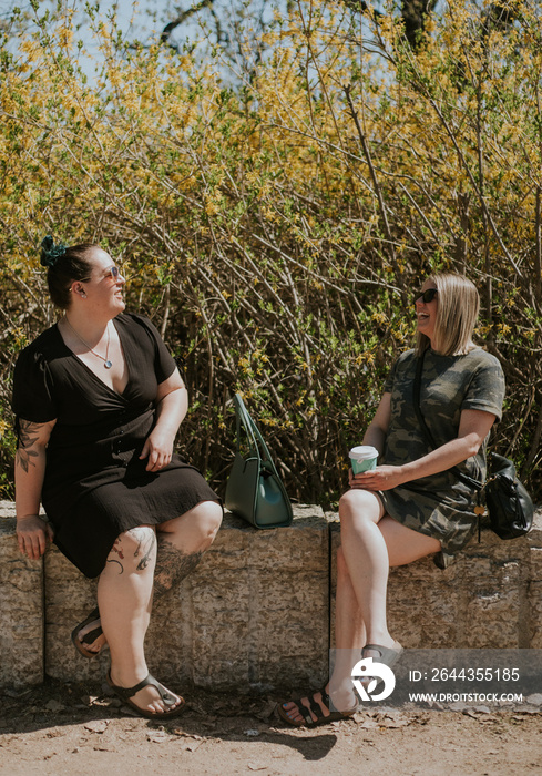 2 women sitting in the park talking and drinking coffee