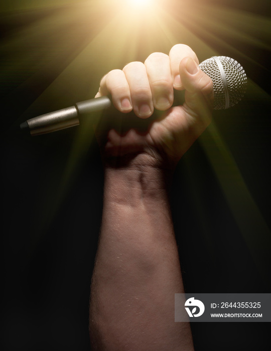 Vertical Microphone Clinched Firmly in Male Fist on a Black Background